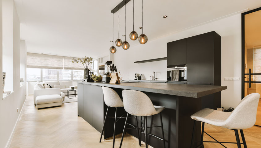 Renovated modern luxury kitchen with black central kitchen island and cabinetry overlooking the living room in an open space.