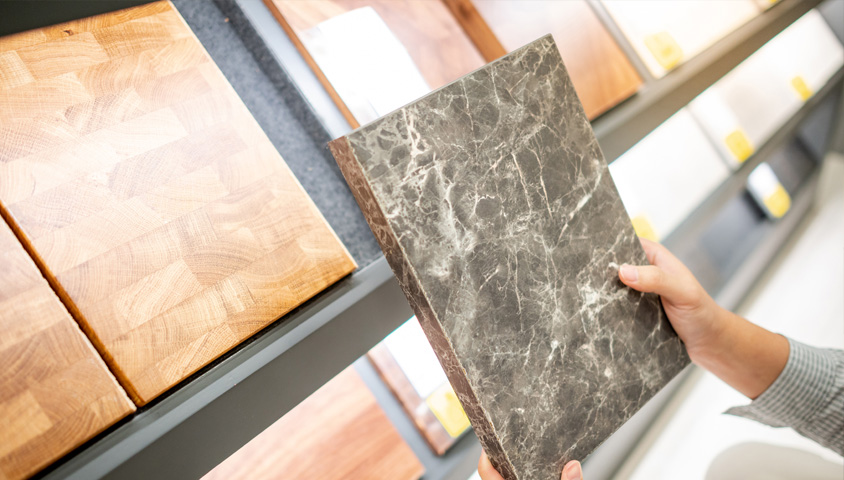 A man holding up a piece of grey marble from a wall of potential materials for a luxury kitchen renovation