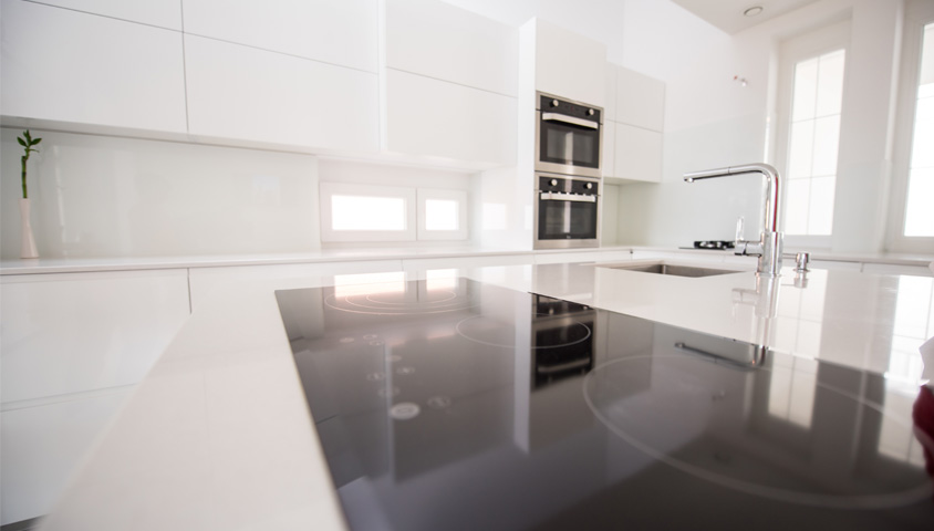 Glossy kitchen countertop and black stovetop up-close inside a white luxury kitchen that recently underwent a kitchen renovation.