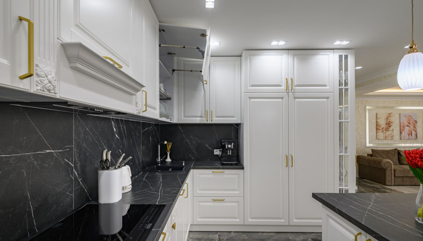 A luxury kitchen with gold embellishments, luxury white cabinetry and a unique black granite bench top and backsplash 