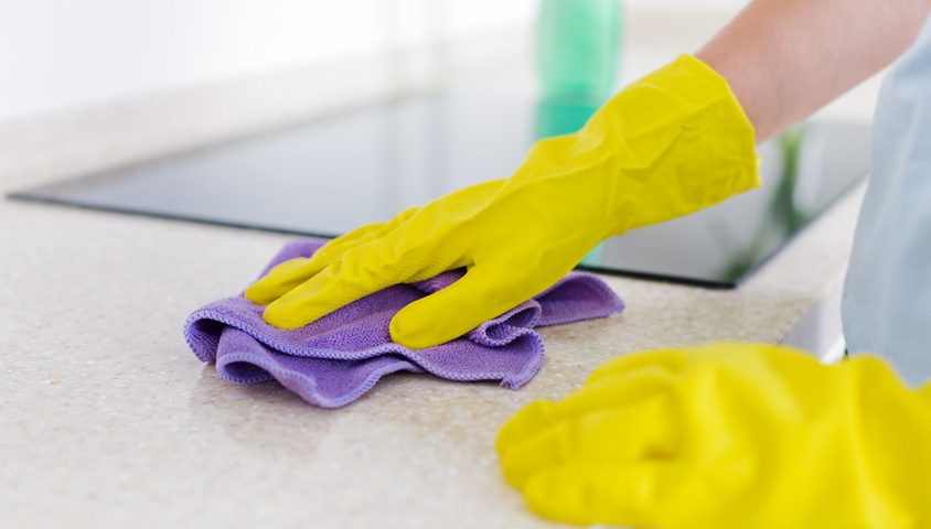 Up-close image of hands with yellow glove cleaning a newly installed white granite kitchen benchtop with cloth