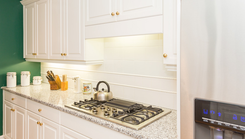 Light grey kitchen counter tops with green feature wall and white cabinetry in a modern renovated home kitchen