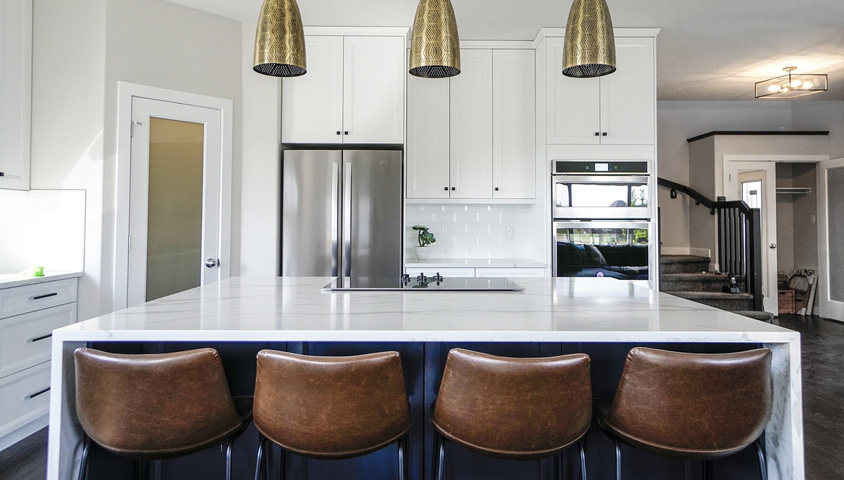 A modern kitchen island with a white countertop inside a newly renovated kitchen with leather bar stools