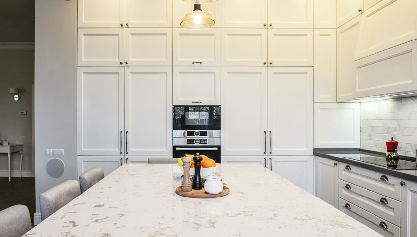 A newly renovated luxury kitchen combining white and grey granite with warm overhead lighting to create a modern and homely feeling.