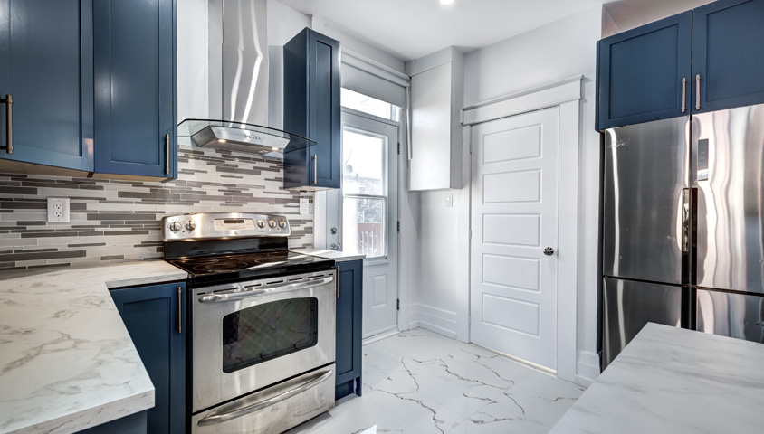 Luxurious blue cabinetry offers a striking contrast against an all-white kitchen, balanced with sleek silver appliances.